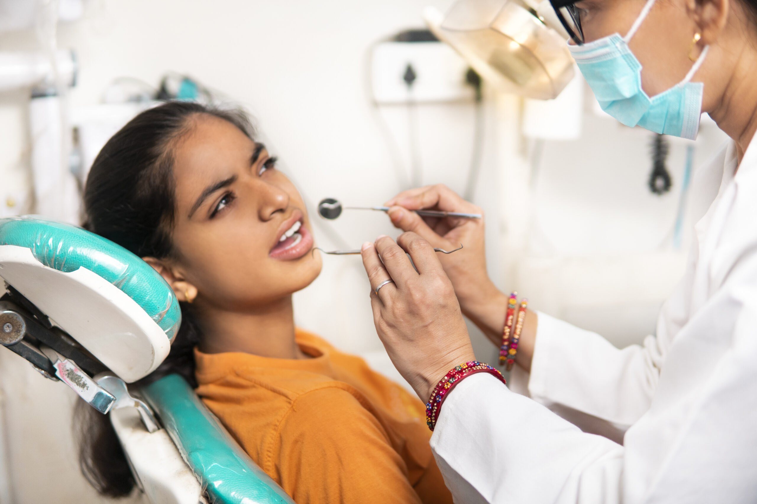 indian-female-young-patient-sitting-chair-with-open-mouth-dentist-examining-her-teeth-with-dental-equipment-clinic